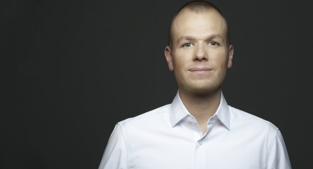 Florian Schütz in weißem Hemd lächelt in die Kamera